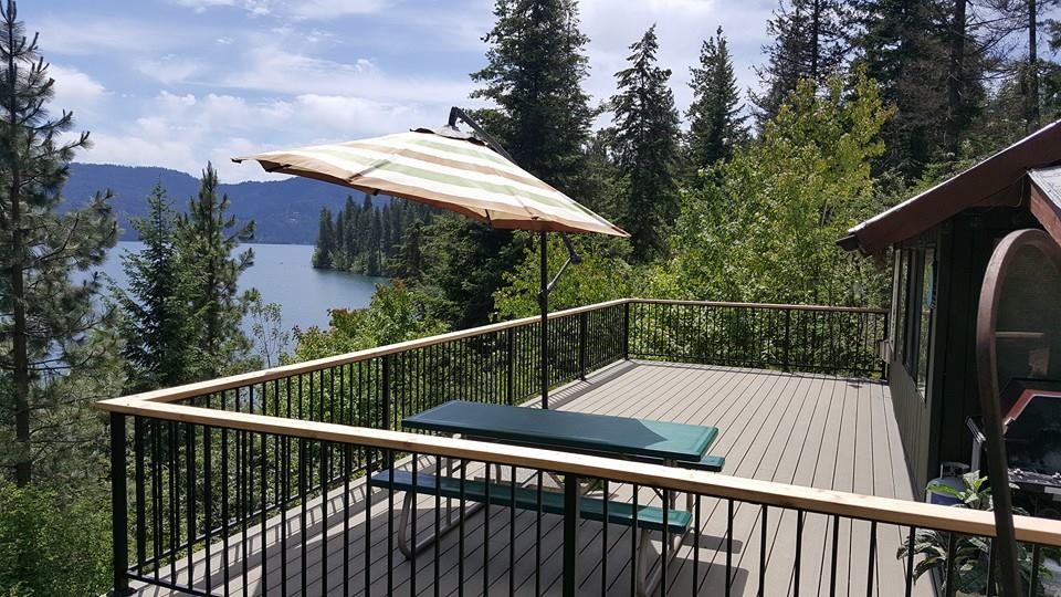 Wooden deck with umbrella and lounge chair overlooking a forested lake and mountains.