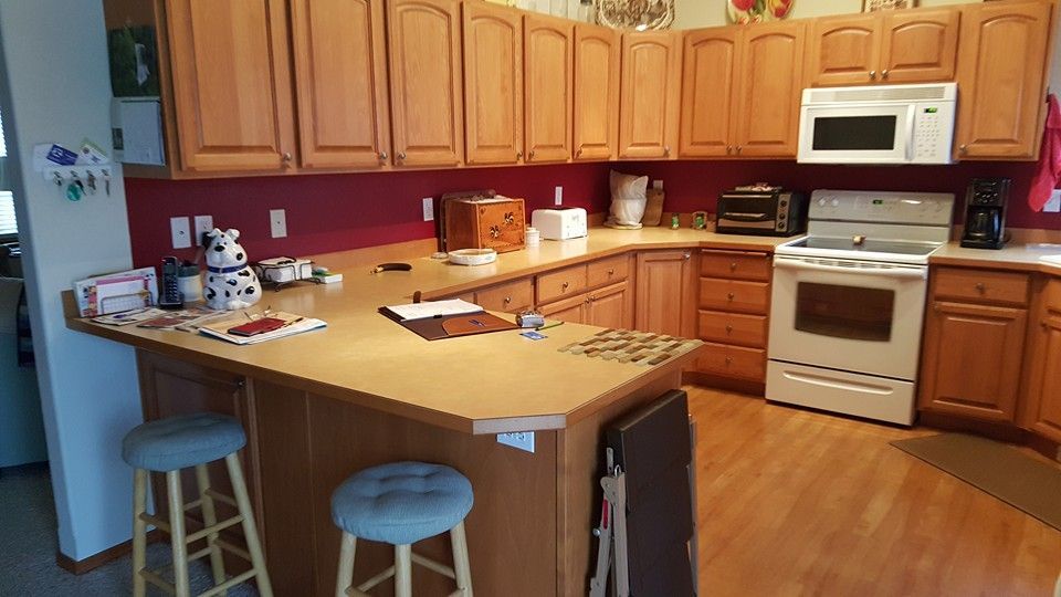 Warm kitchen with wooden cabinets, white appliances, and a breakfast bar with stools.
