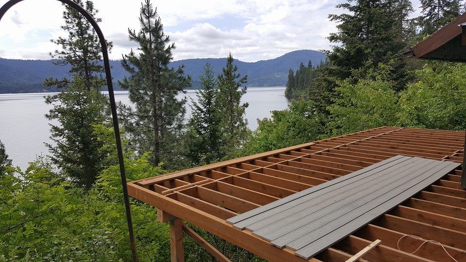 Wood deck overlooking a lake and forested mountains, with a gray board resting on the railing