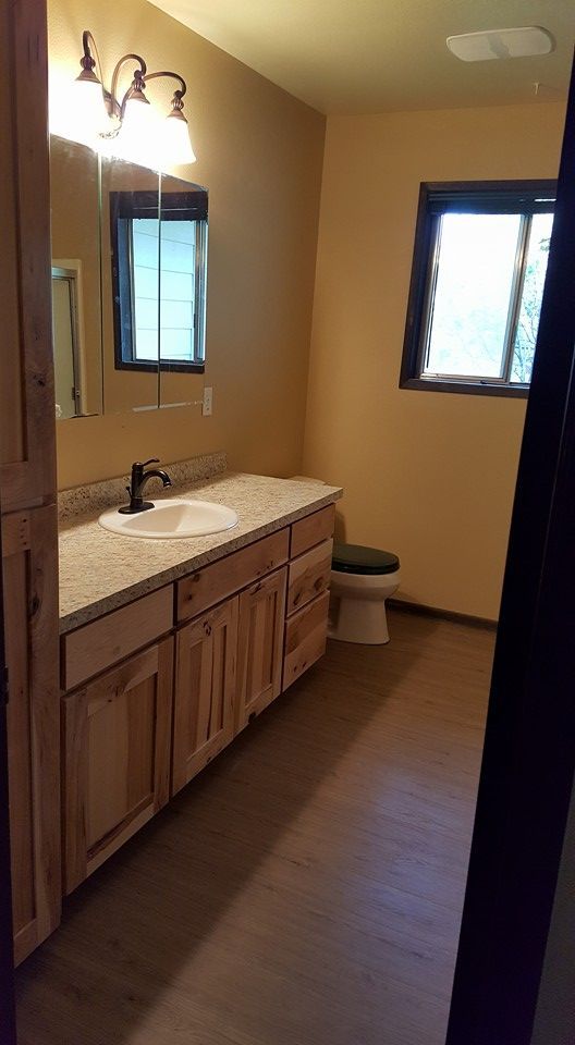 Small bathroom with wooden vanity, sink, mirror, and two windows, viewed from the doorway