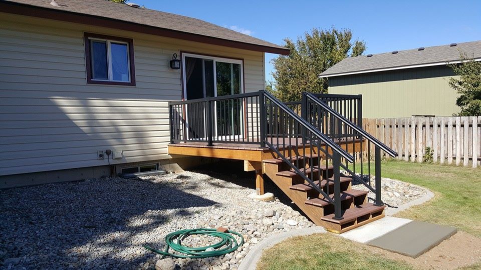 Backyard deck with stairs beside a beige house and a coiled green hose on gravel.