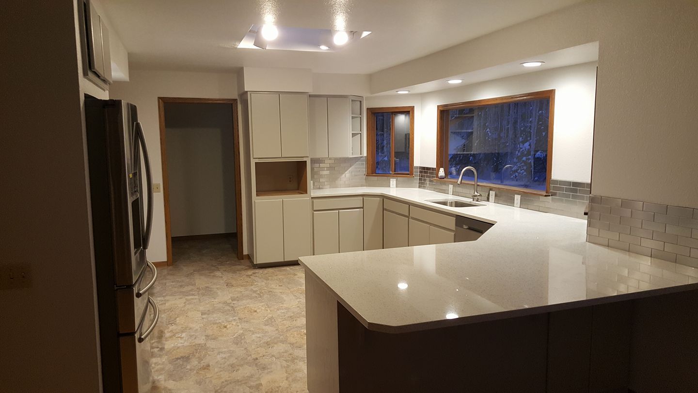 Empty modern kitchen with white cabinets, granite island, and large window at night