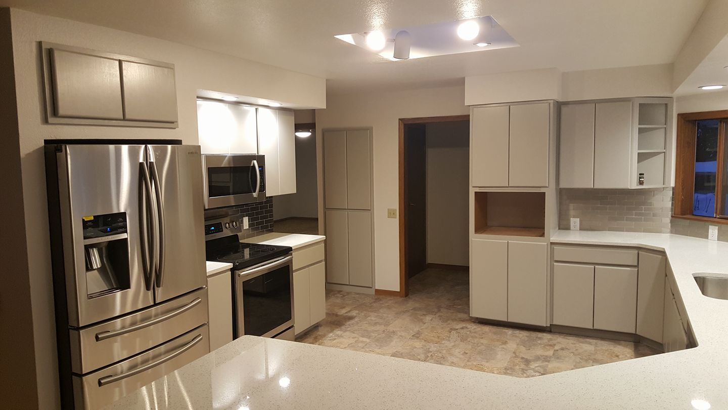 Modern kitchen with stainless steel fridge, white cabinets, stove, and island under bright ceiling lights
