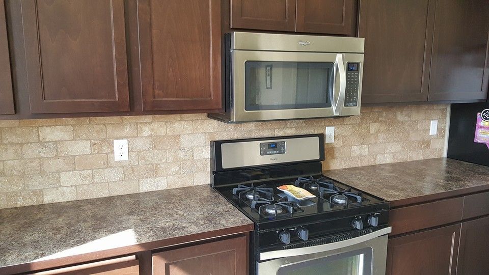 Kitchen with dark wood cabinets, granite countertop, stainless microwave, and gas stove against a beige tile backsplash