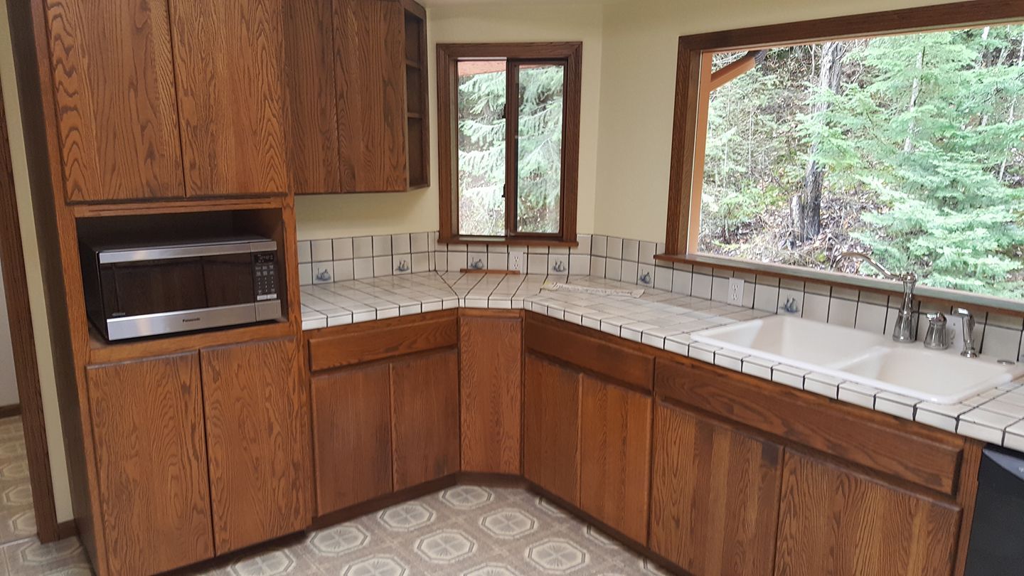 Kitchen with wood cabinets, white tile counters, and large windows overlooking trees