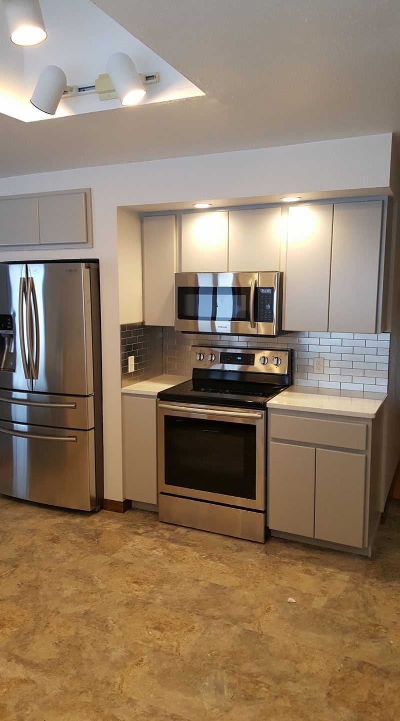 Modern kitchen with stainless steel appliances, white cabinets, and beige tile flooring