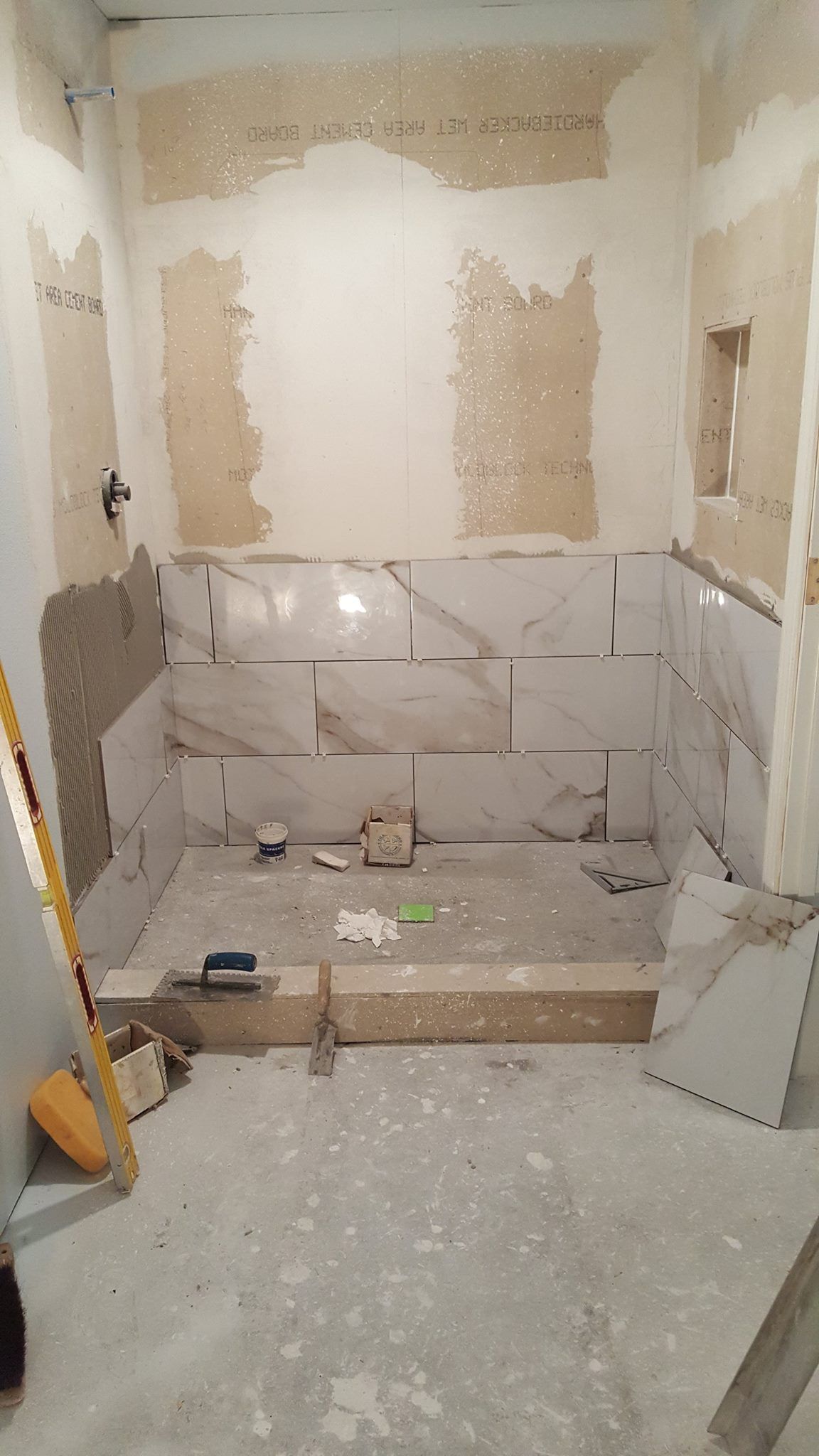 Partially renovated bathroom with exposed drywall, tiled lower walls, and construction debris on the floor
