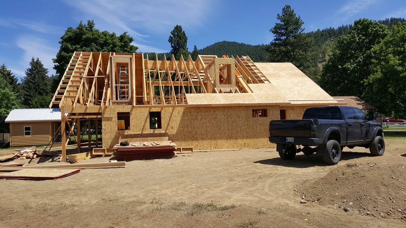 Partially built wooden house under construction with a black pickup truck on a dirt lot