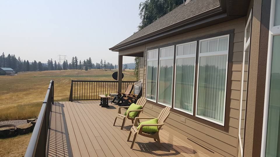Wooden deck beside a house with patio chairs and a wide view of a grassy field.