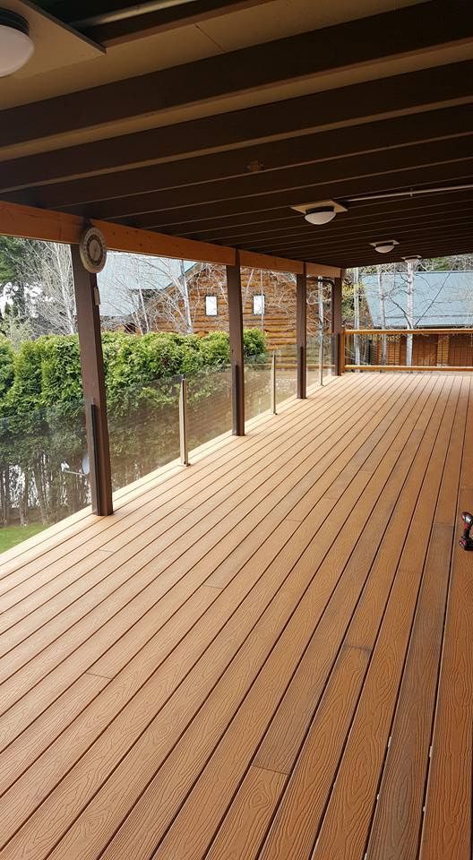 Covered wooden deck with exposed beams, railing, and garden view beyond the columns.