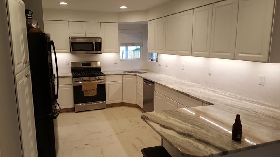 Bright modern kitchen with white cabinets, stainless appliances, and a long light stone countertop.