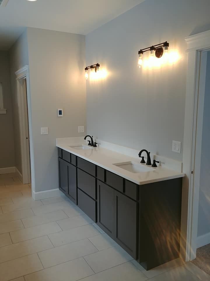 Modern double-sink bathroom vanity with black cabinets, white countertop, and wall sconces.