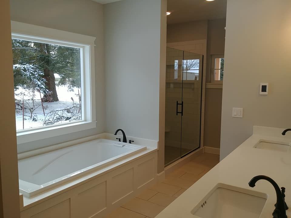 Modern bathroom with white soaking tub, glass shower, double sinks, and a snowy window view