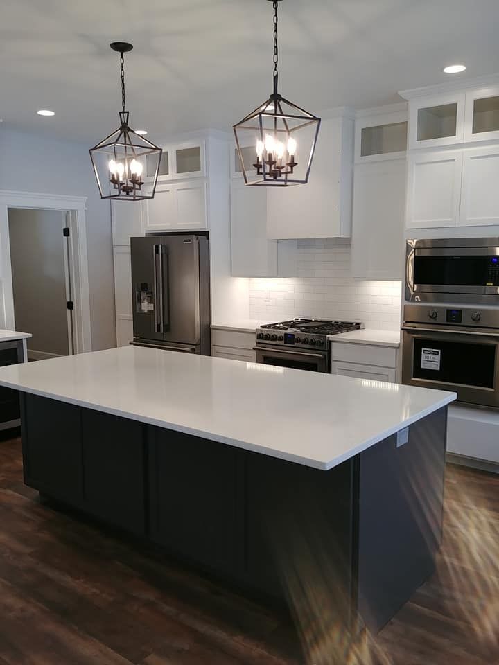 Modern kitchen with white cabinets, stainless appliances, dark floor, and large island under pendant lights