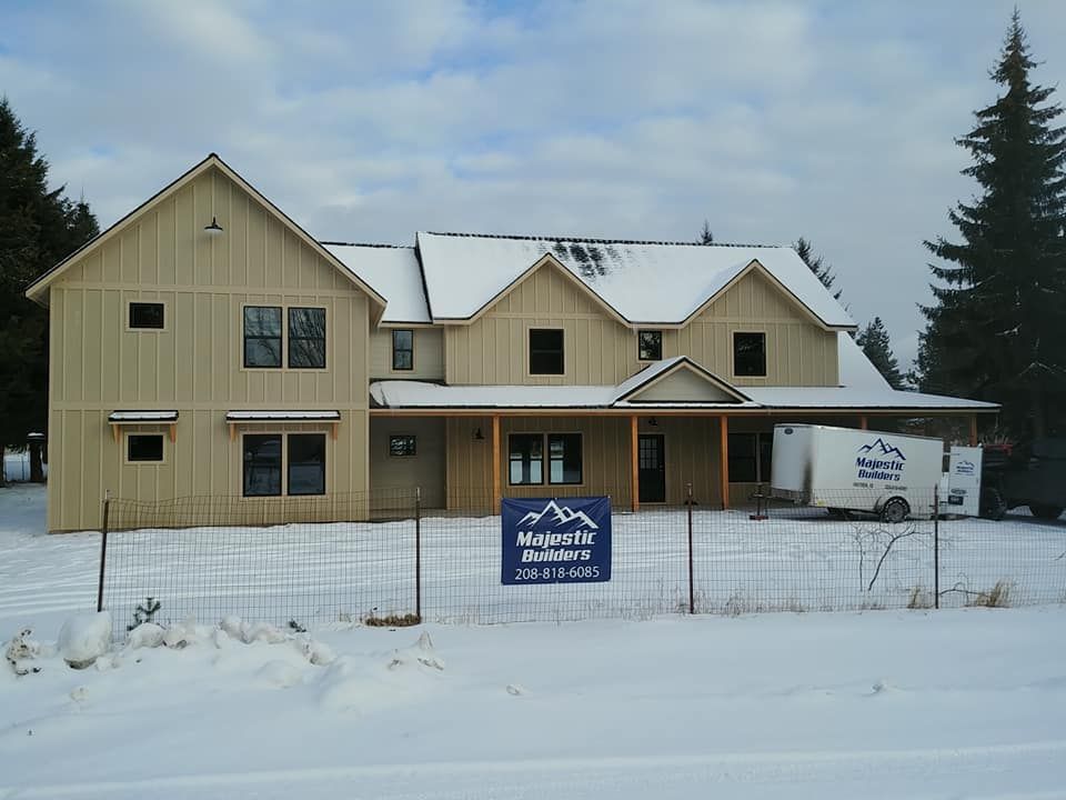 Snowy front view of a beige house with a covered porch and a real estate sign in the yard