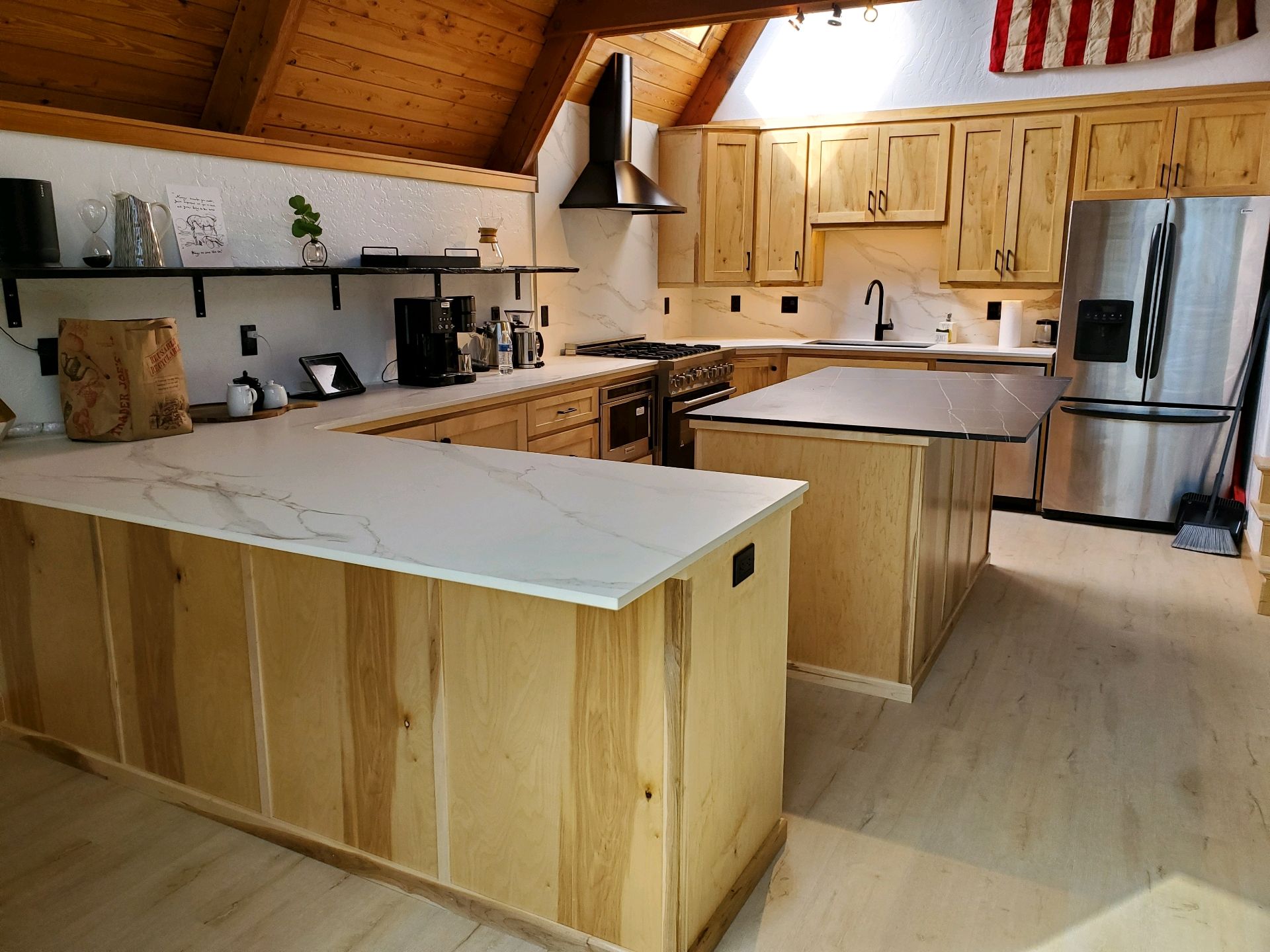 Wooden cabin kitchen with pine cabinets, white island, stainless stove, and exposed beams