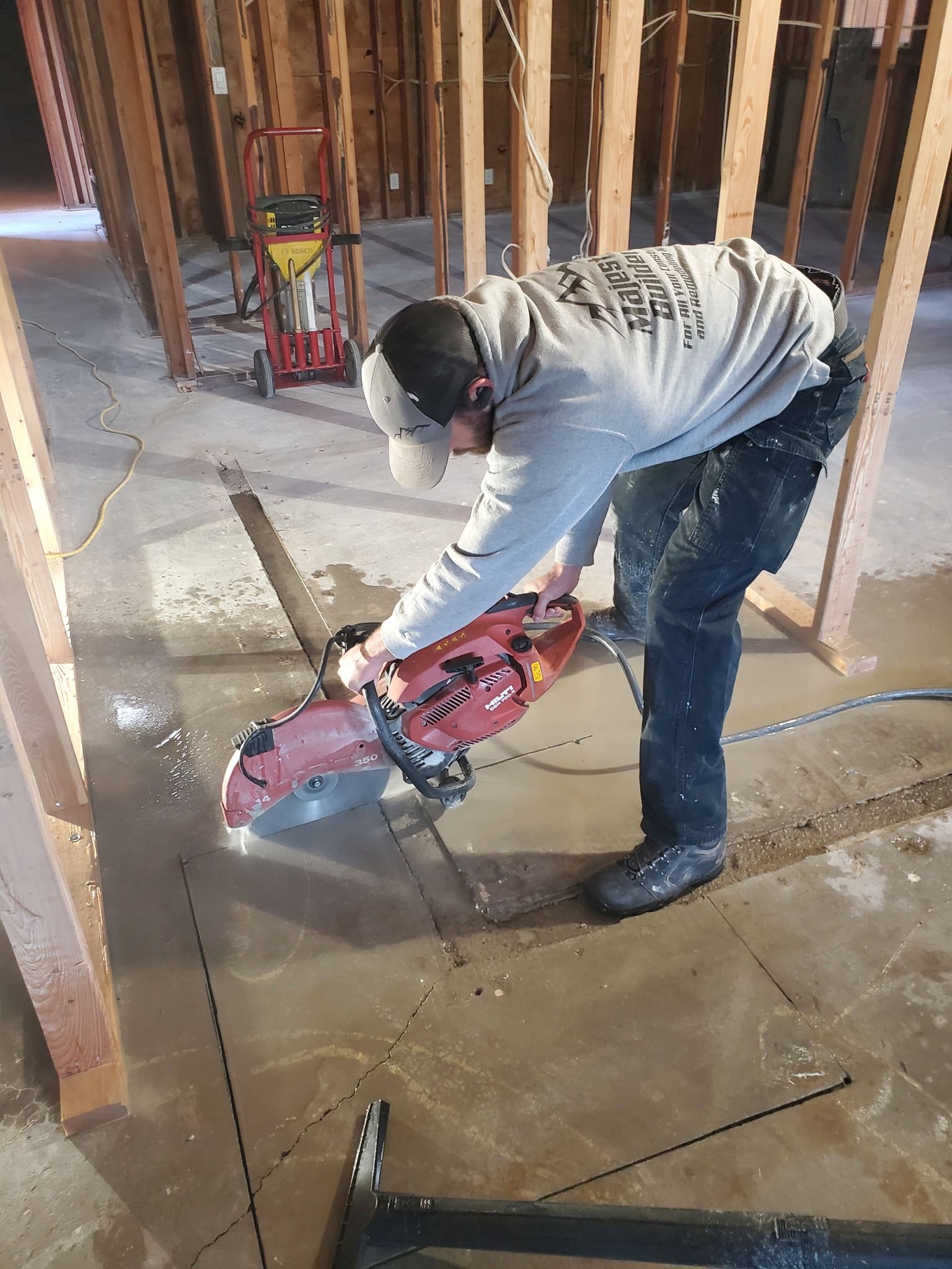 Worker using a red concrete saw to cut a floor slab inside a framed construction site