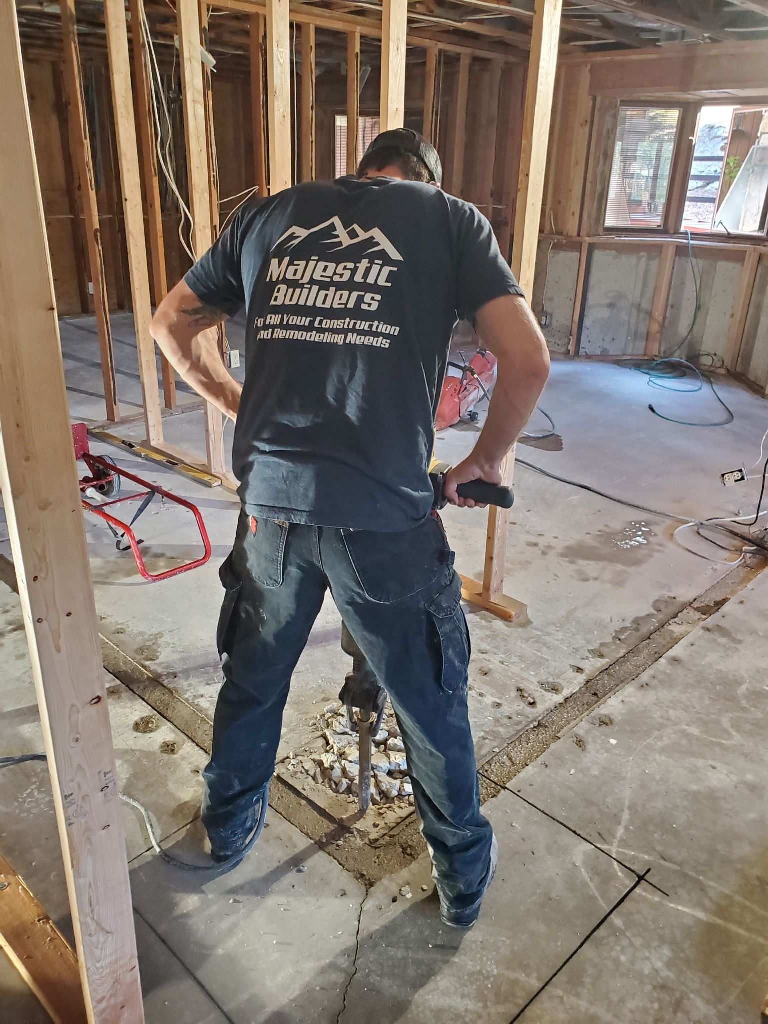 Worker using a power tool in an unfinished room with exposed studs and debris on the floor