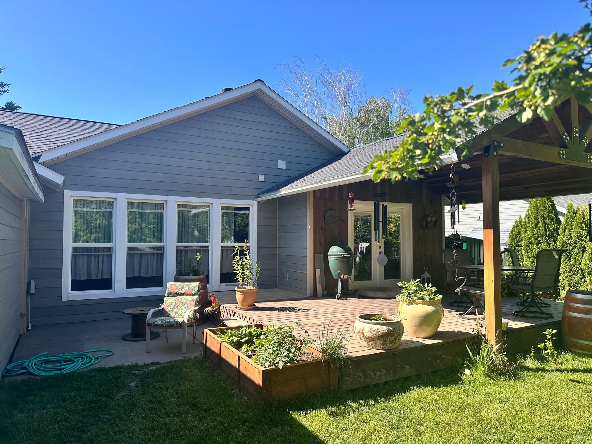 Backyard patio with raised wooden deck, pergola, potted plants, and a house with white-trimmed windows