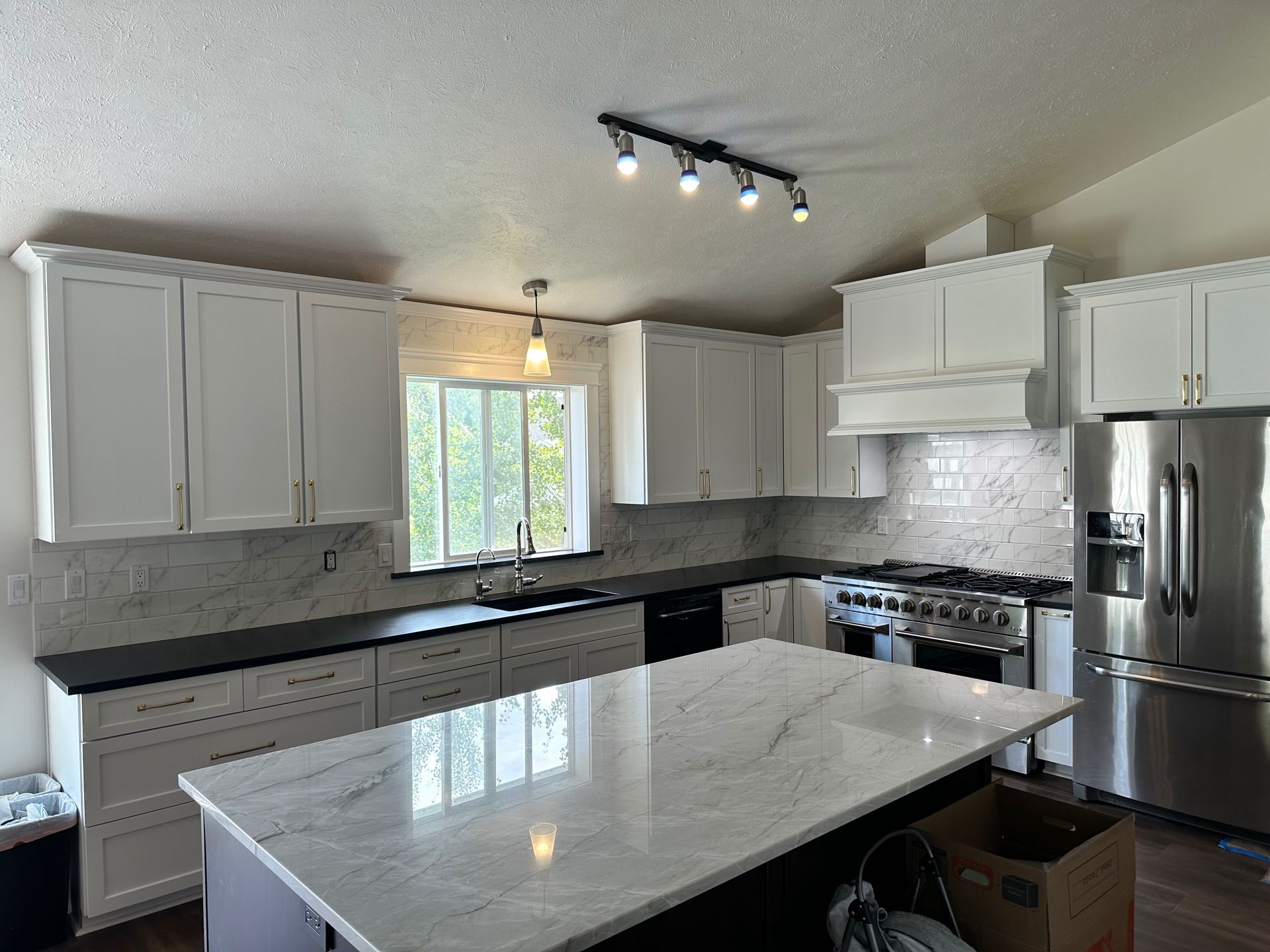 Modern kitchen with white cabinets, stainless steel appliances, dark countertops, and a large island