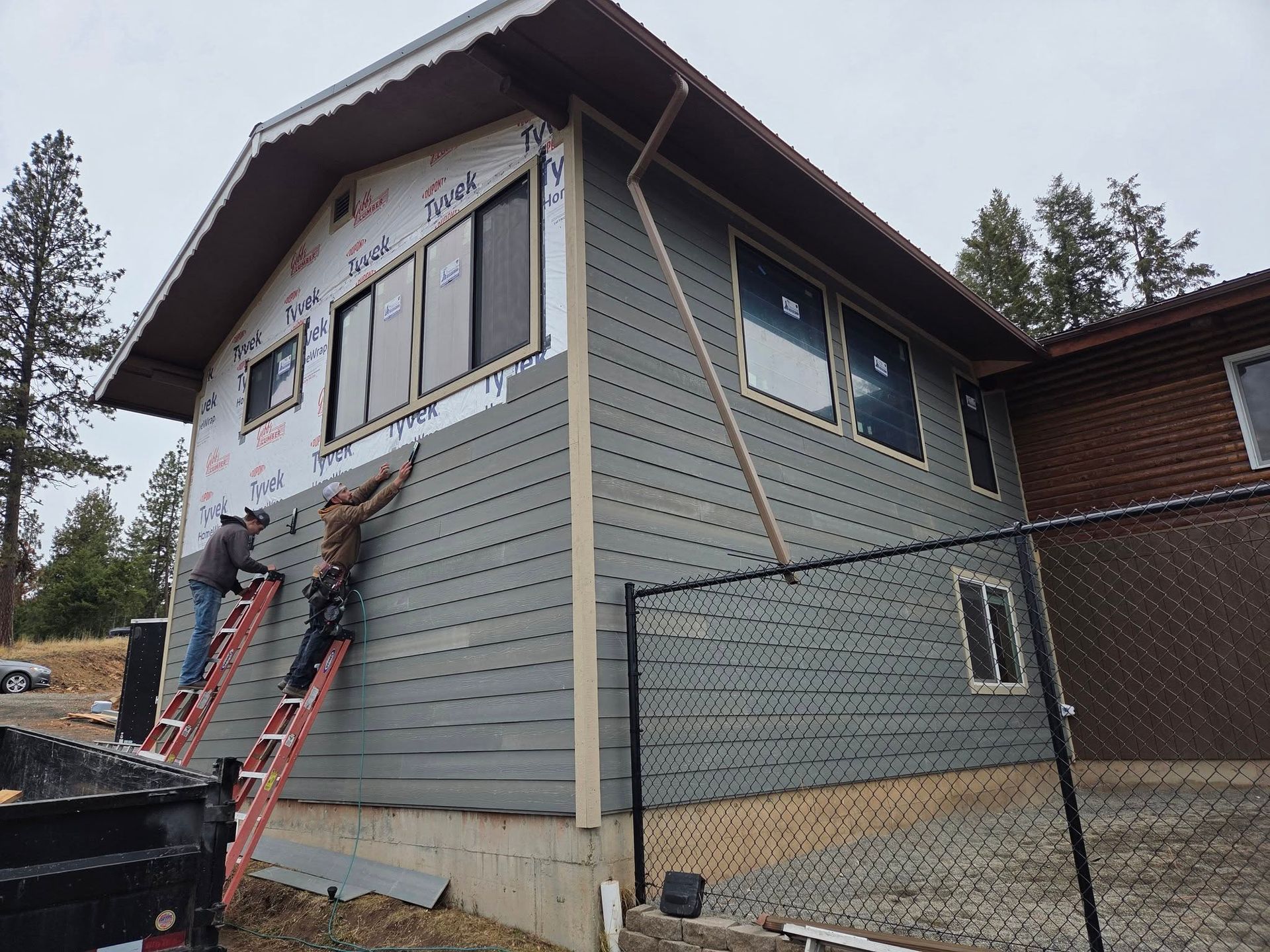 Partially finished house with ladders, scaffolding, and workers installing exterior siding