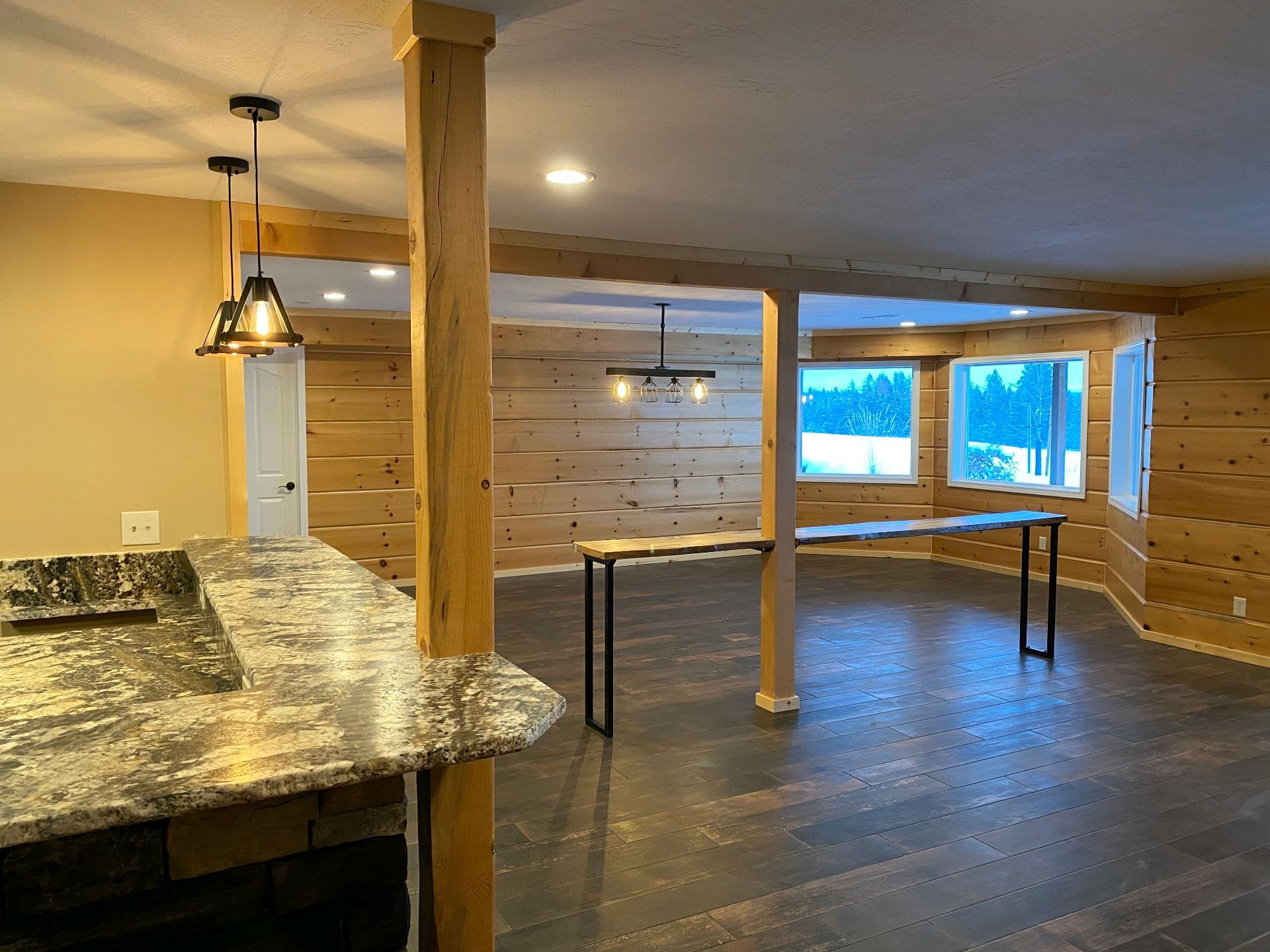 Rustic open-concept room with wood beams, a granite counter, and large windows overlooking snowy outdoors