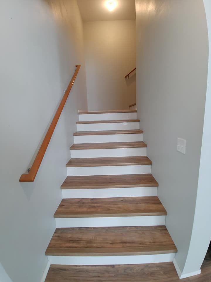 Narrow indoor staircase with white walls, wooden handrail, and light wood steps leading upstairs