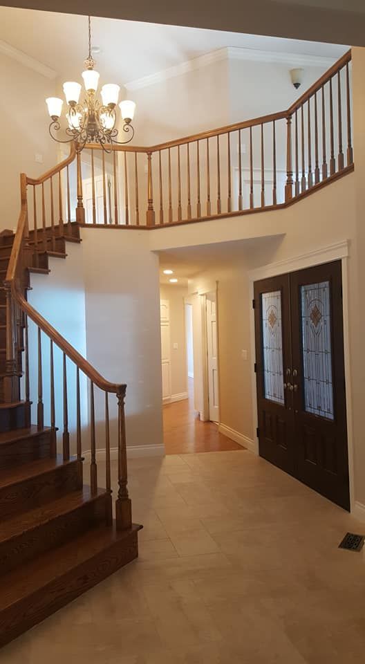 Spacious foyer with curved staircase, wood railing, chandelier, and double front doors