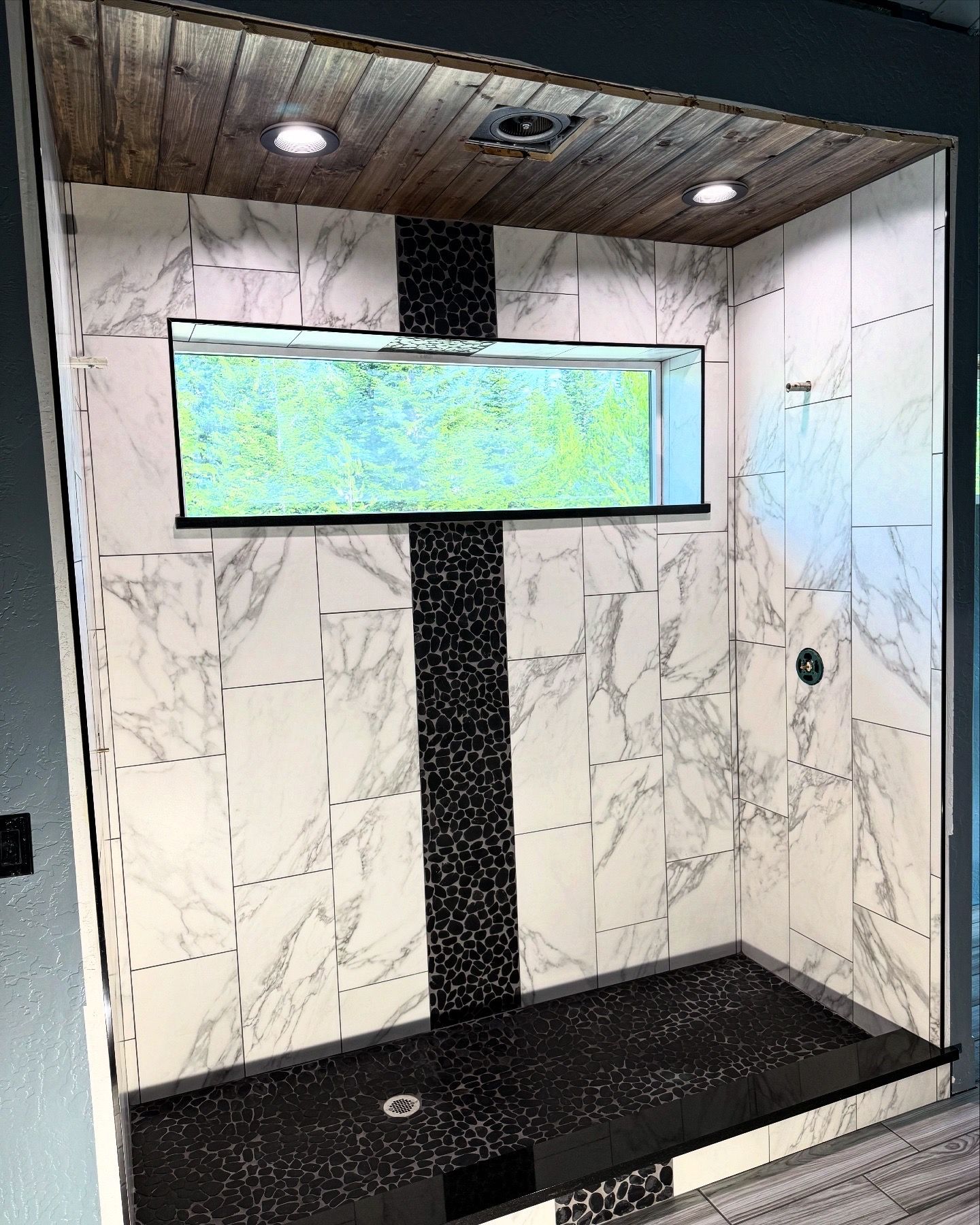 Modern shower nook with marble-look walls, black tile bench, and a horizontal window under recessed lights