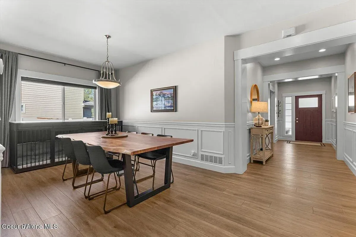 Bright dining room with wooden table, chairs, chandelier, and hallway into a lit entryway