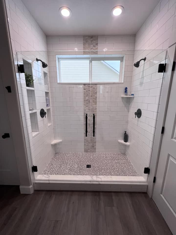 Spacious walk-in shower with white tile, glass doors, built-in niches, and pebble shower floor.
