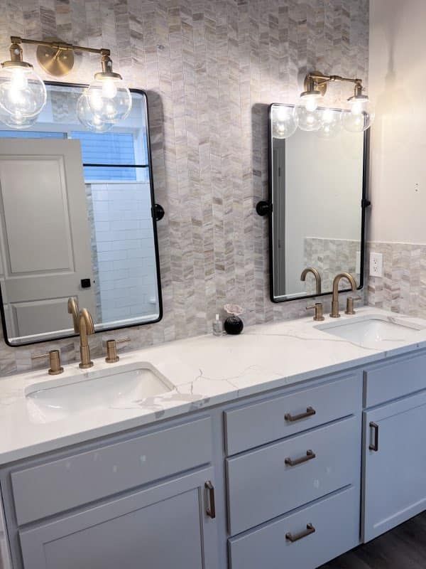 Bathroom vanity with two mirrors, brass sconces, white countertop, and gray cabinets.
