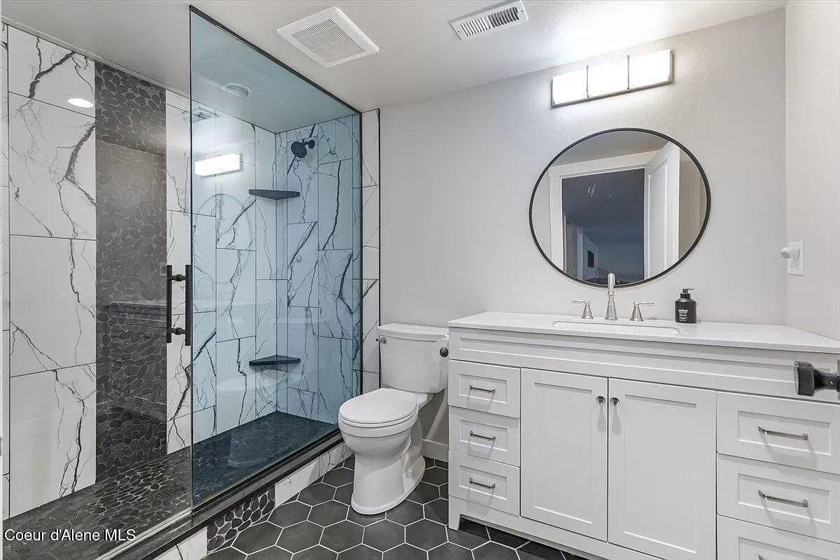 Modern bathroom with glass shower, toilet, and white vanity with round mirror