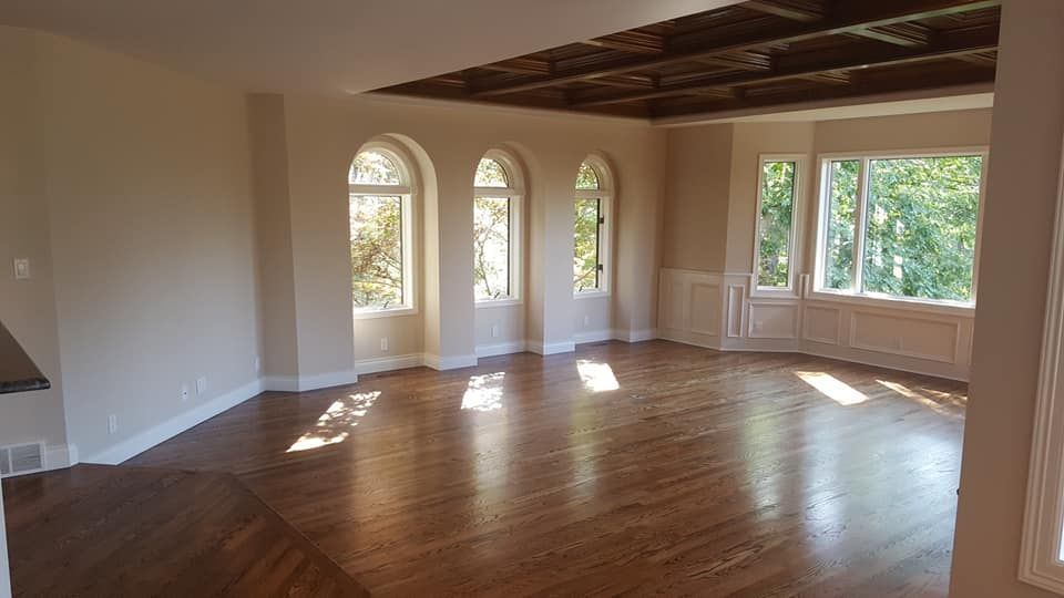 Empty living room with hardwood floors, arched windows, and sunlight streaming in