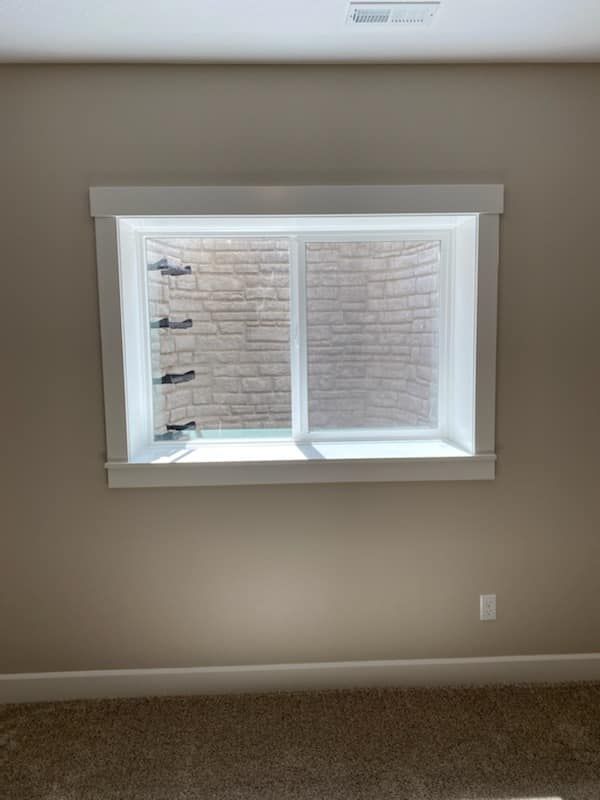 Empty beige room with a small white-framed window and carpeted floor