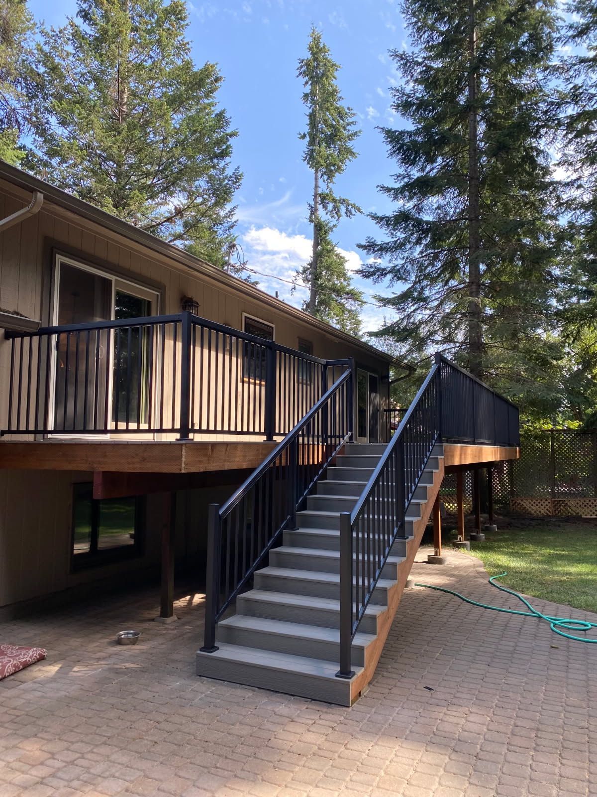 Wooden deck with stairs leading to a raised house among tall pine trees