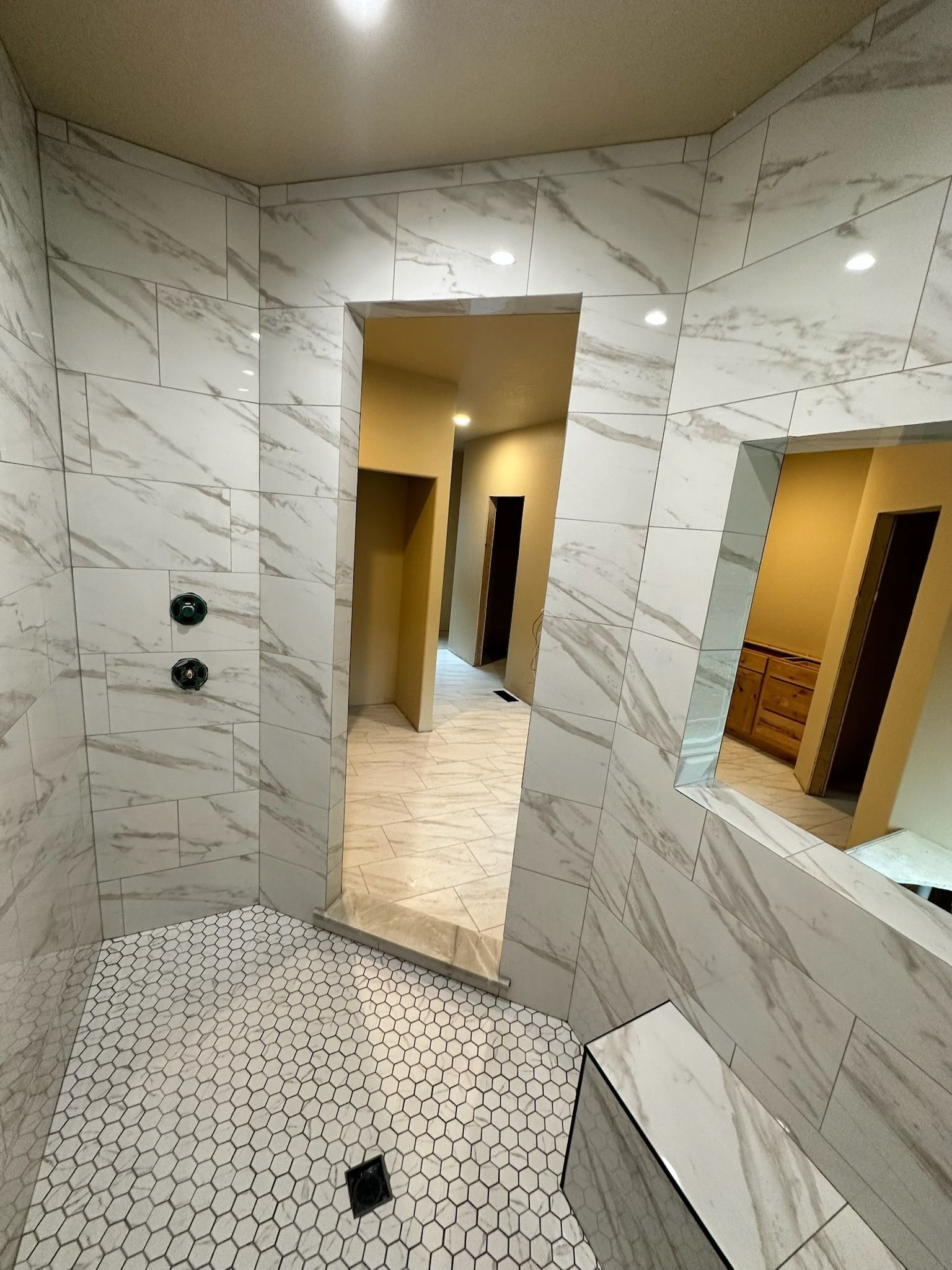 Marble-tiled bathroom with walk-in shower, mosaic floor, and open doorway to a tiled hall