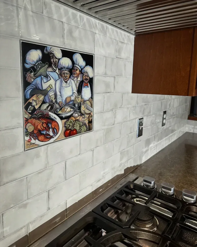 Kitchen backsplash with a chef-themed tile mural above a gas stovetop and counter.