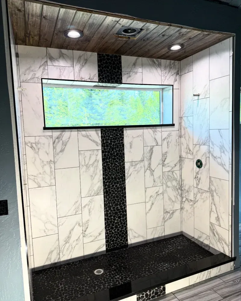 Modern tiled shower with black bench, marble-look walls, and illuminated niche shelf