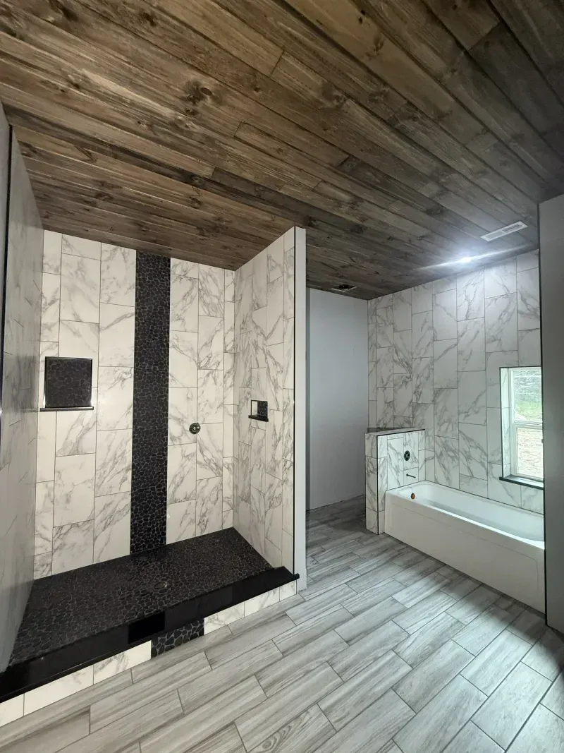 Modern bathroom with marble-look walls, dark wood ceiling, walk-in shower, and windowed tub area