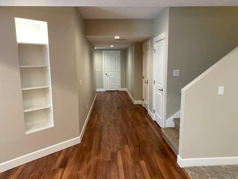 Empty hallway with wood floors, beige walls, built-in shelf, and staircase on the right.