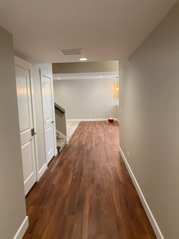 Empty hallway with white walls, wood floors, and a small red object at the far end.