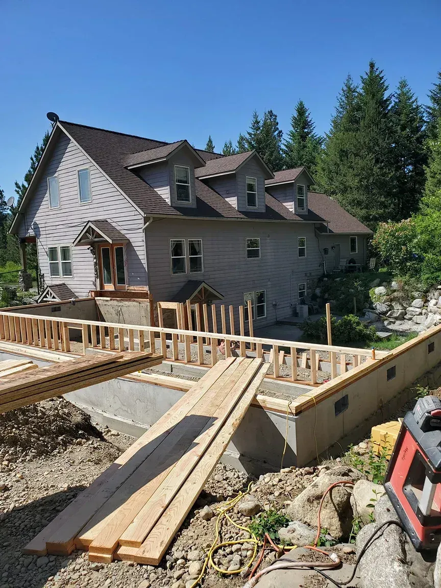 House under construction with wooden foundation framing and planks in the foreground under a clear blue sky