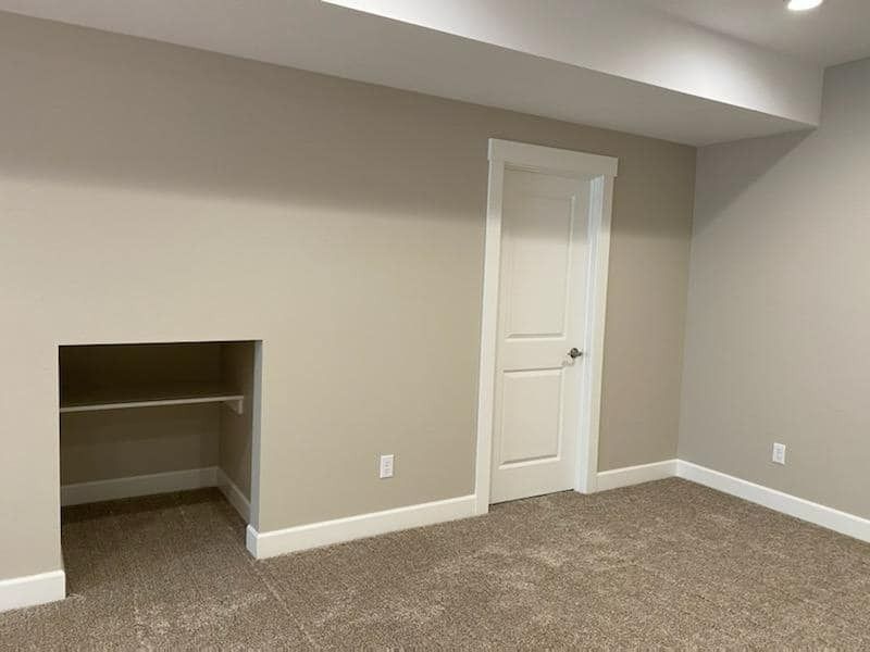 Empty beige room with carpet, a small closet opening, and a white door under a sloped ceiling.
