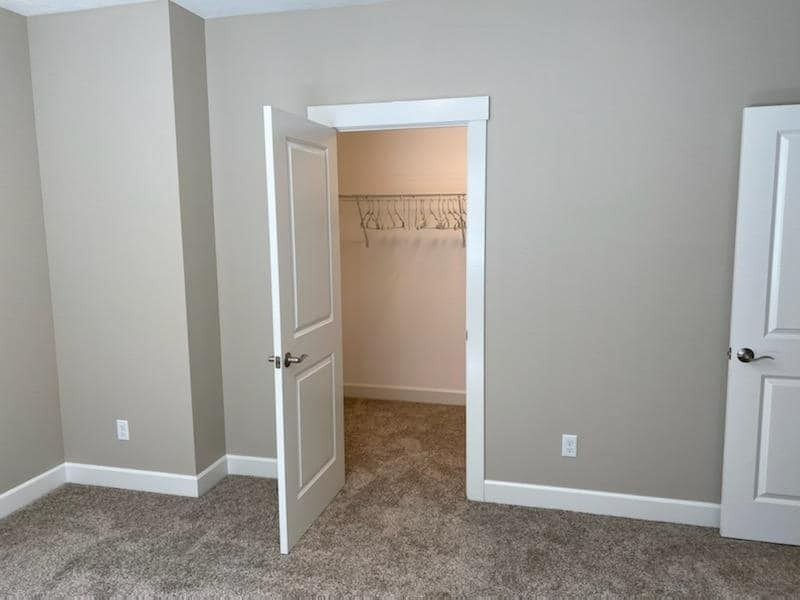 Empty beige bedroom with open closet doors and carpeted floor