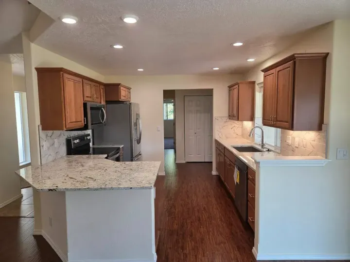 Empty modern kitchen with wood cabinets, granite counters, stainless appliances, and recessed lighting