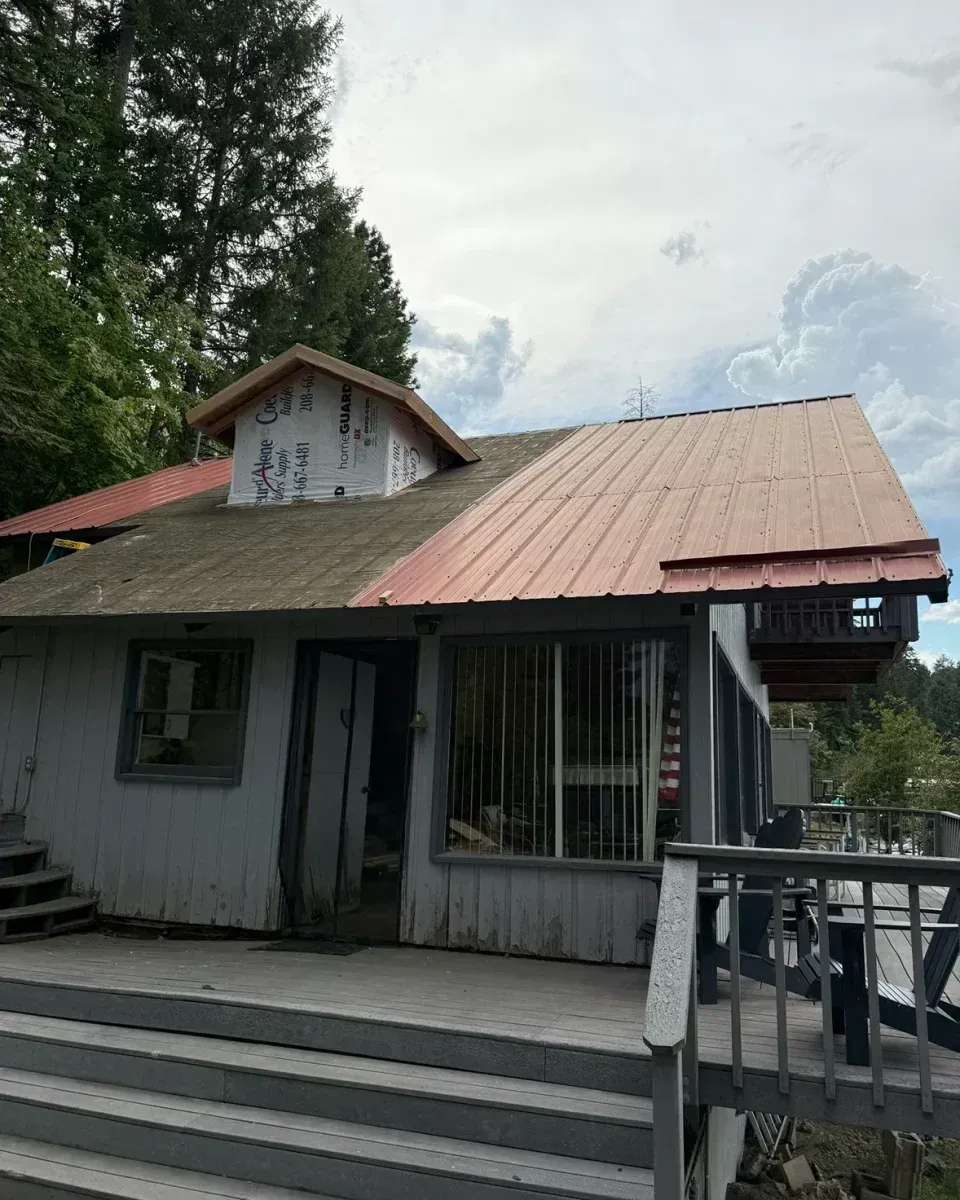 Small white building with a rust-red roof, steps, and a porch railing under a cloudy sky.