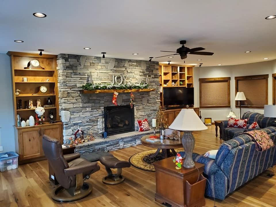 Cozy living room with stone fireplace, blue sofa, wood chairs, and built-in shelves