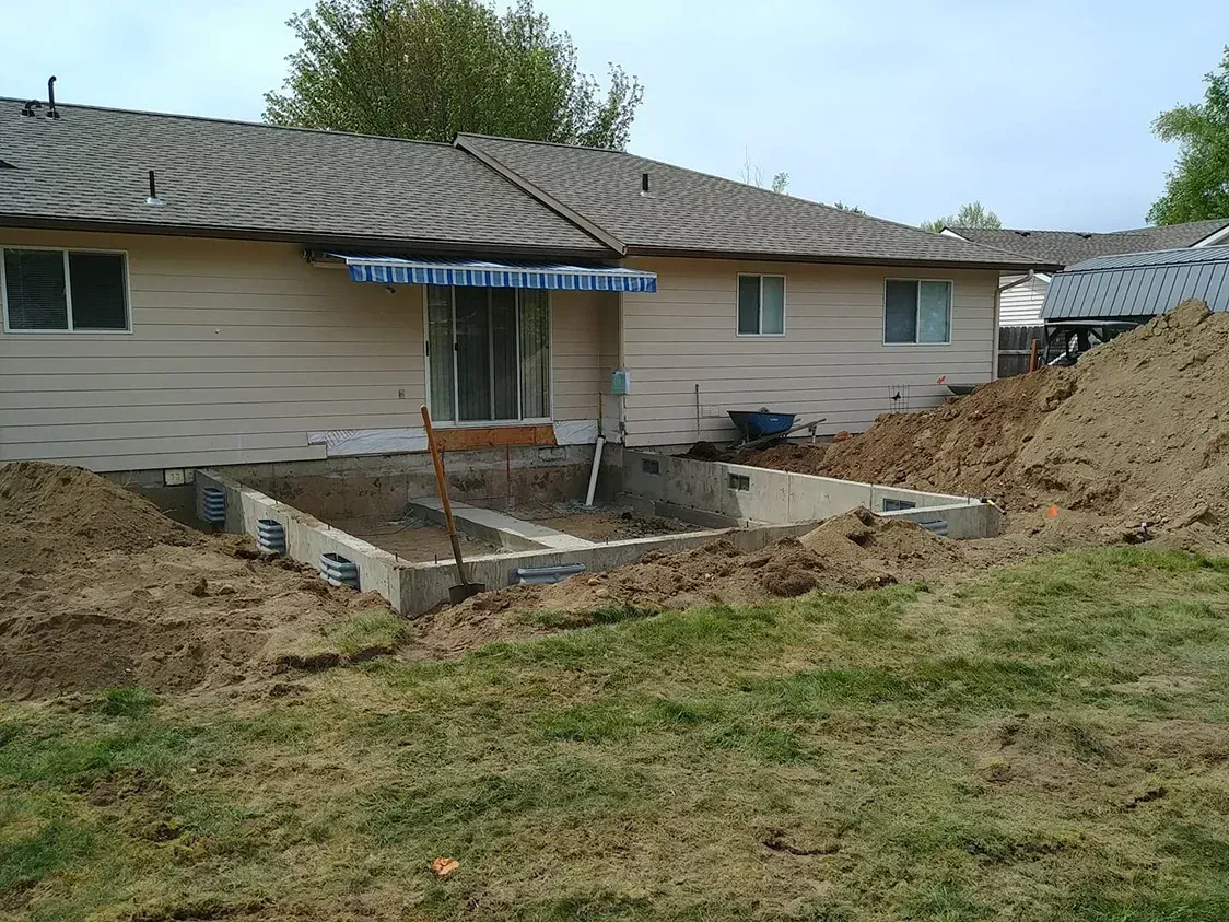 House with large dirt excavation and foundation work in the yard, suggesting ongoing construction or repair