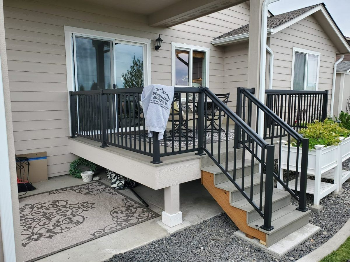 Front porch with black railings and steps, beige siding, and a sign hanging on the porch railing.
